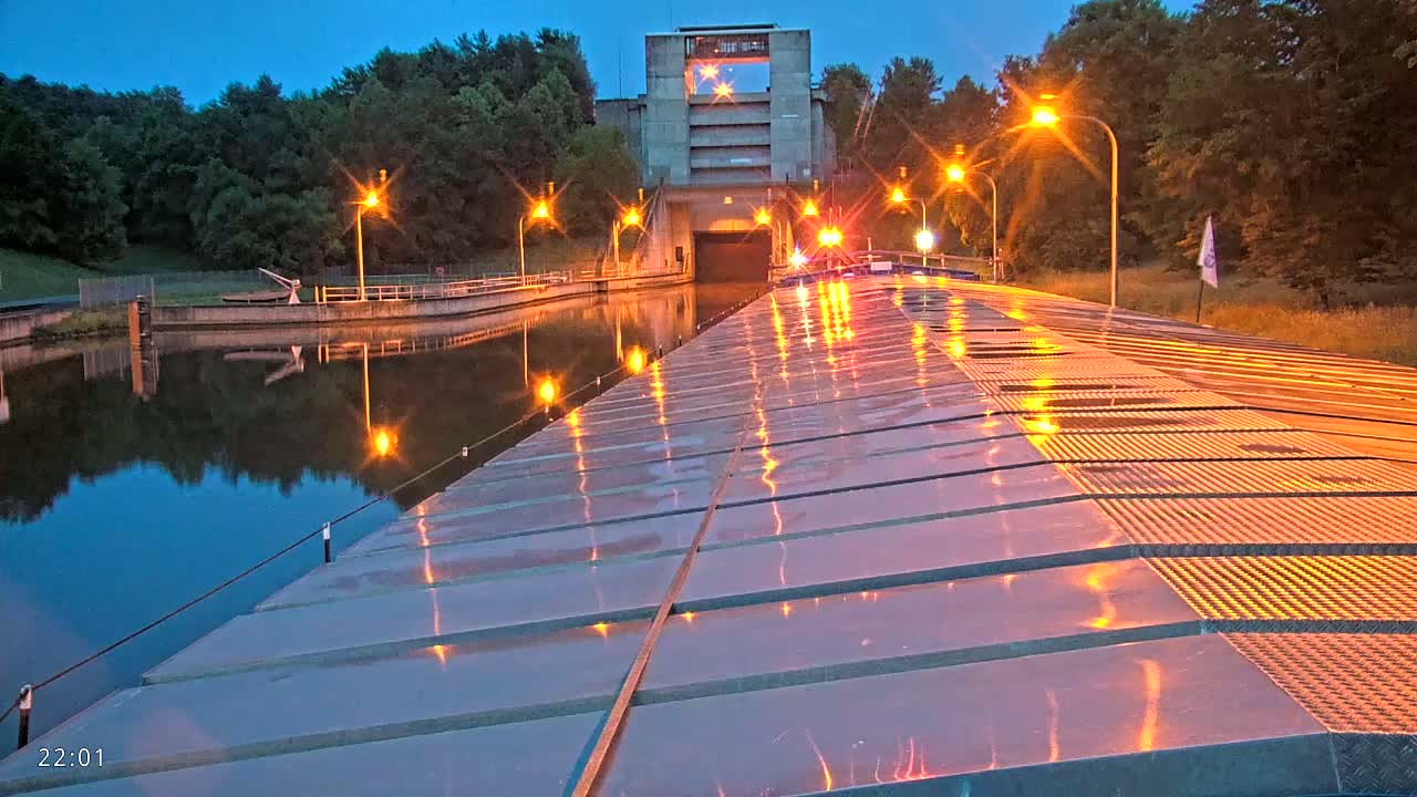 A wet, illuminated canal lock at twilight, with a large concrete structure at the far end and trees lining the banks.