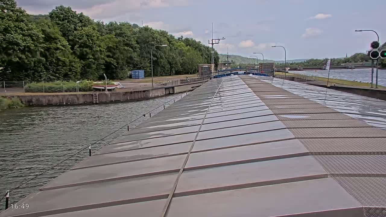 A barge's deck stretches towards a canal lock under a partly cloudy sky.