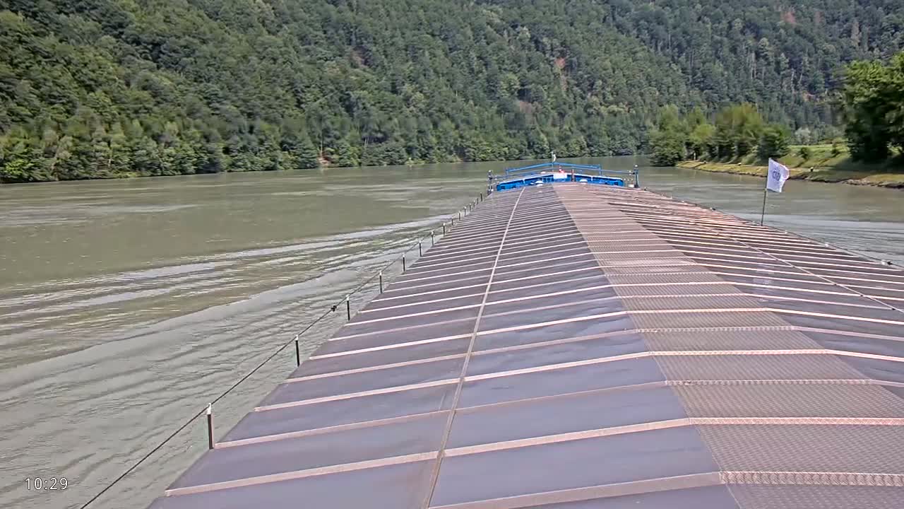 A barge travels down a wide river bordered by lush green hills under a calm sky.