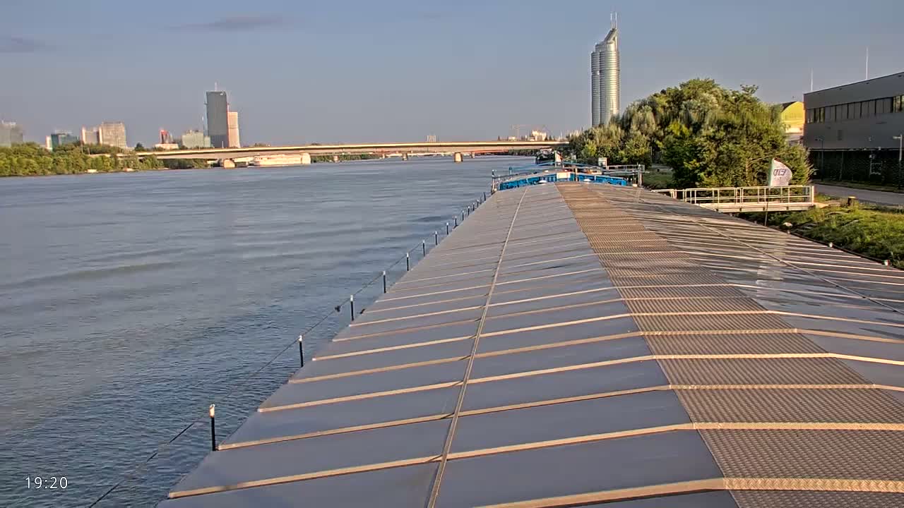 A barge's deck stretches toward a cityscape on a calm river under a clear sky.