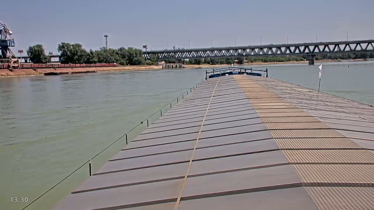 A barge travels down a river on a sunny day, passing under a bridge.
