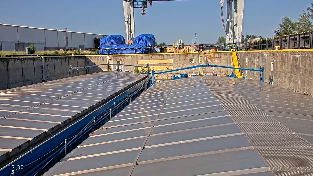 The image shows the flat, gray, paneled roof of a barge or ship in a lock, under sunny skies.