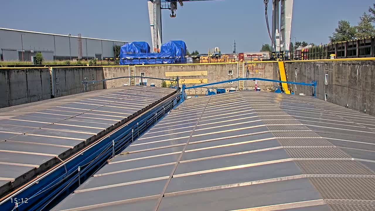 A view from above shows two long, parallel sections of a flat, gray surface with metal grating walkways, situated within a concrete dock on a sunny day.