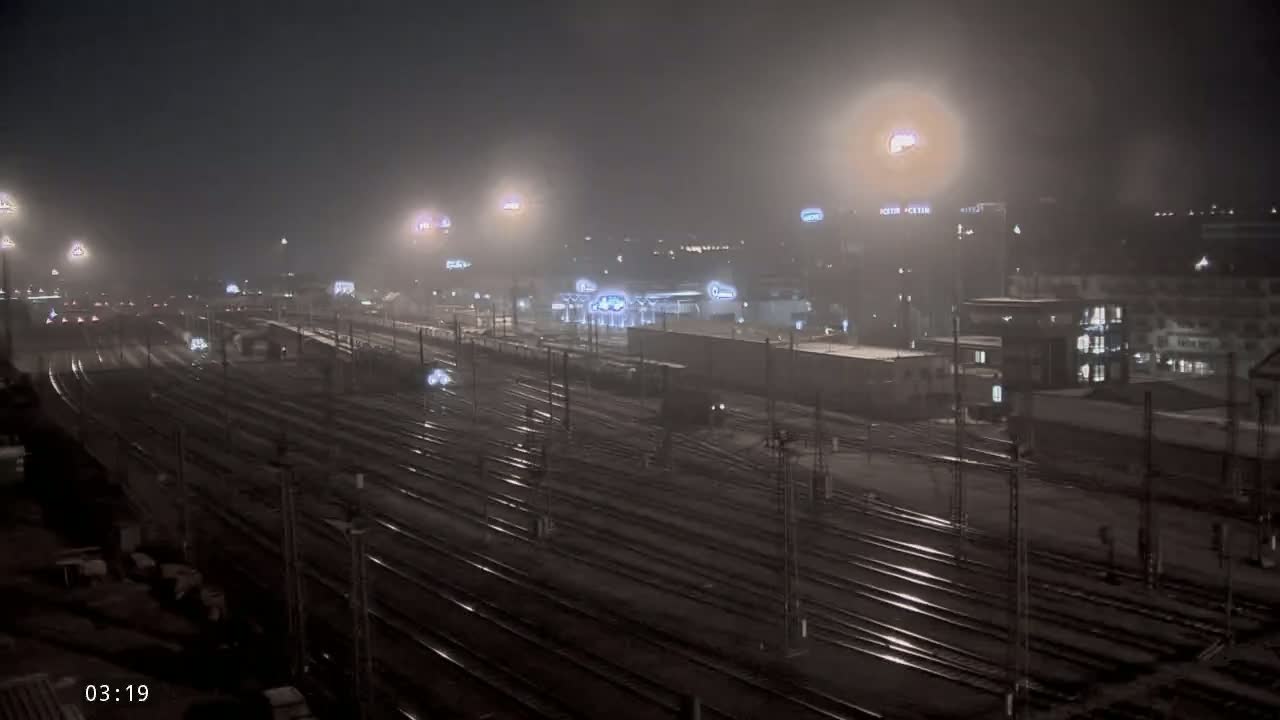 A nighttime view of a train yard with numerous tracks under foggy conditions.