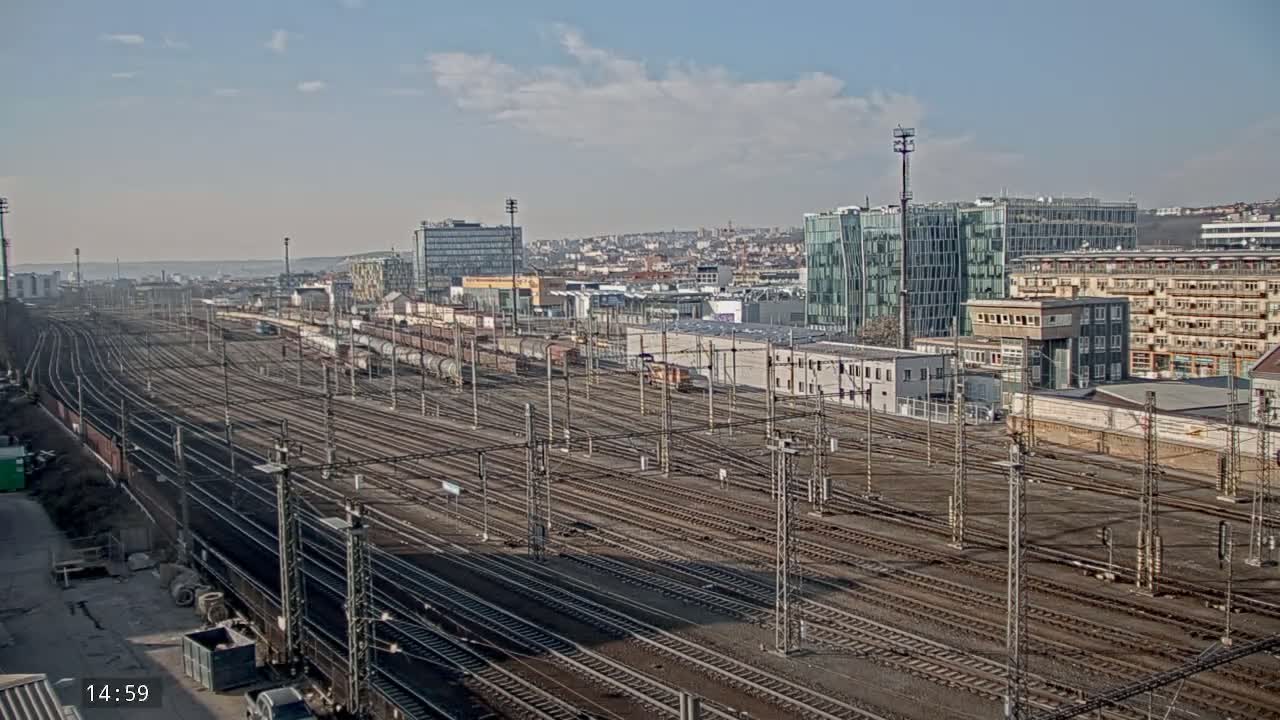 A sprawling railway yard with numerous tracks extends to a cityscape under a partly cloudy sky.