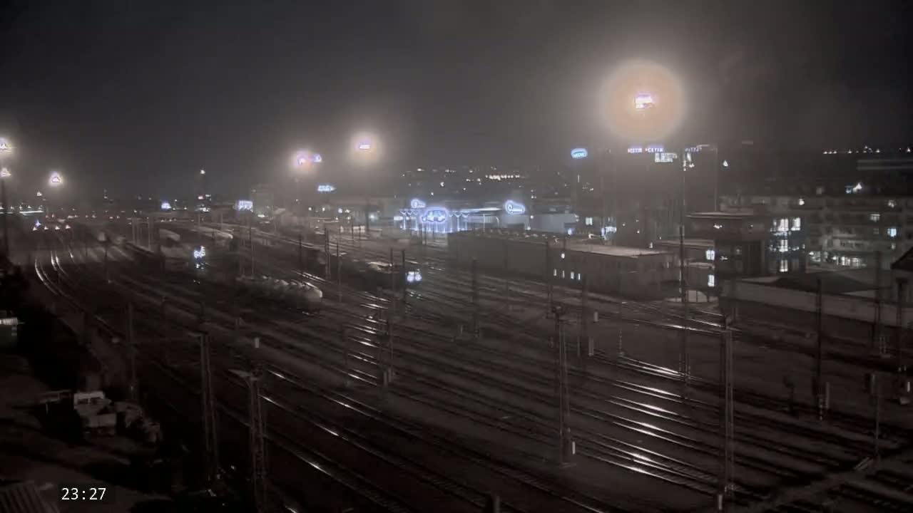 A nighttime, hazy view of a sprawling train yard with numerous tracks, illuminated by artificial lights.