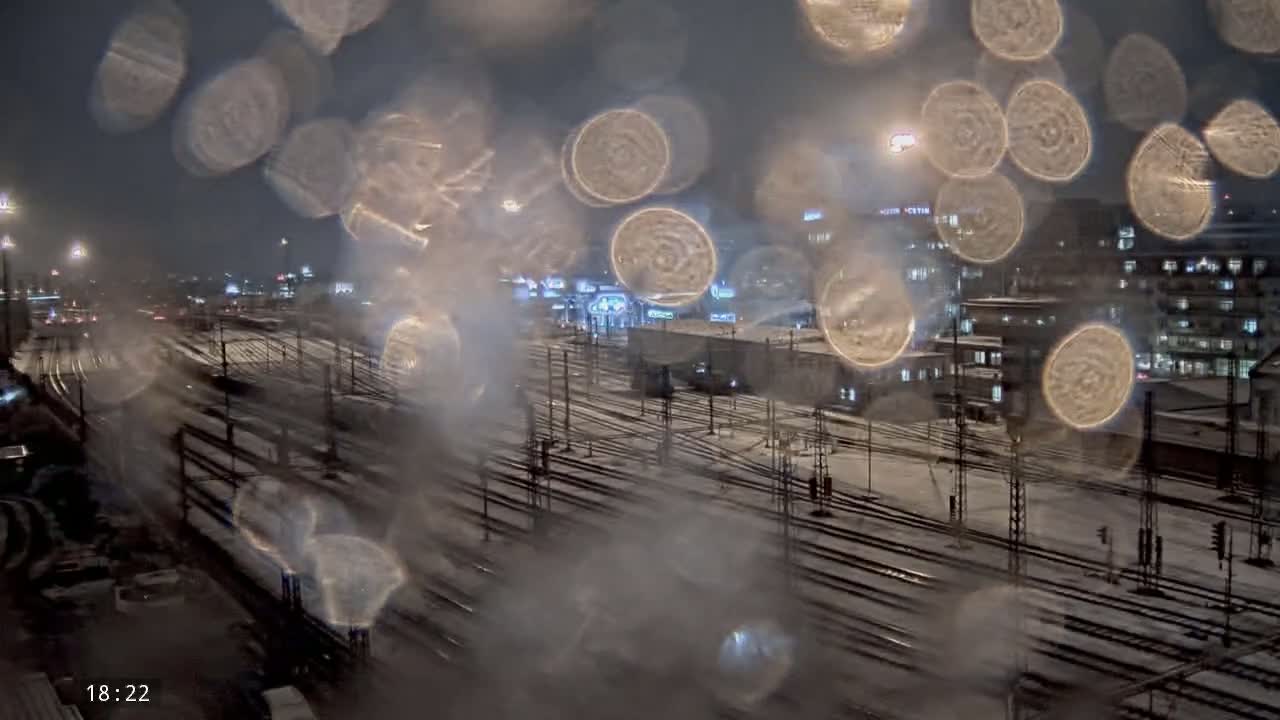 A snowy nighttime view of a railway yard, seen through a rain-covered window.