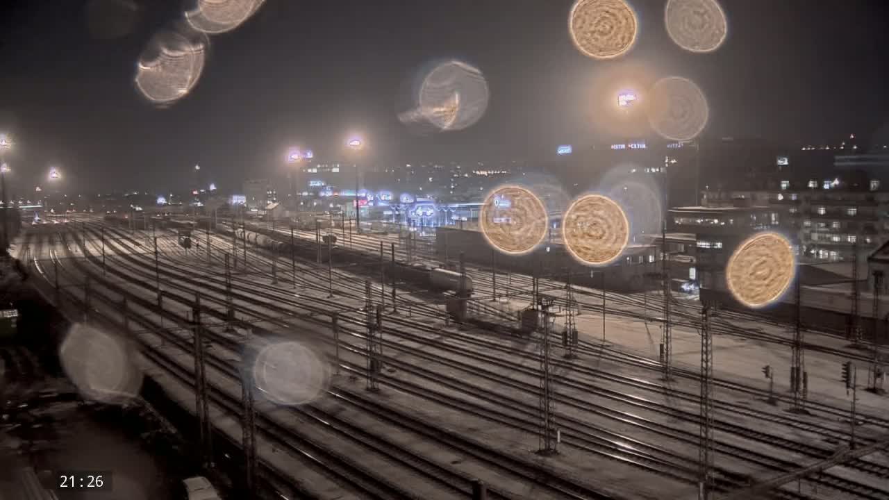 A snow-covered train yard at night, viewed from above, with blurry water droplets obscuring the view.