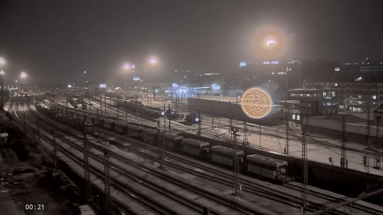 A snowy train yard at night, illuminated by streetlights, with several trains visible on numerous tracks.