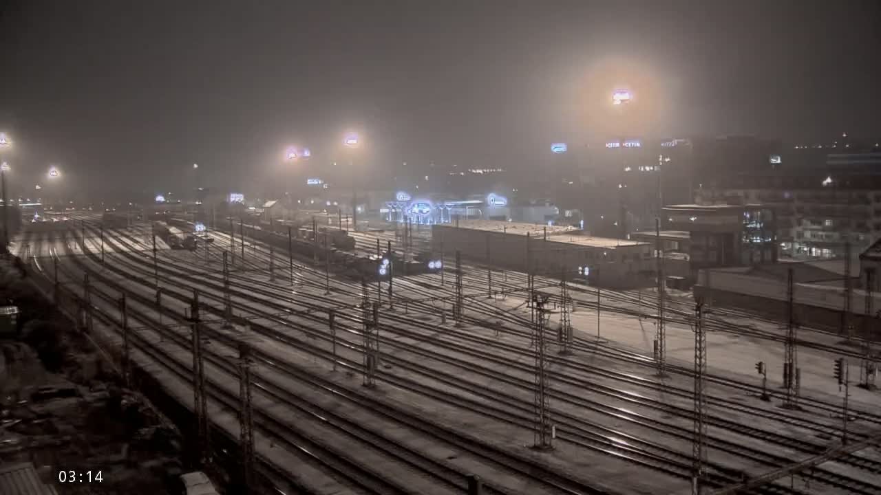 A snow-covered train yard at night, illuminated by artificial lights.