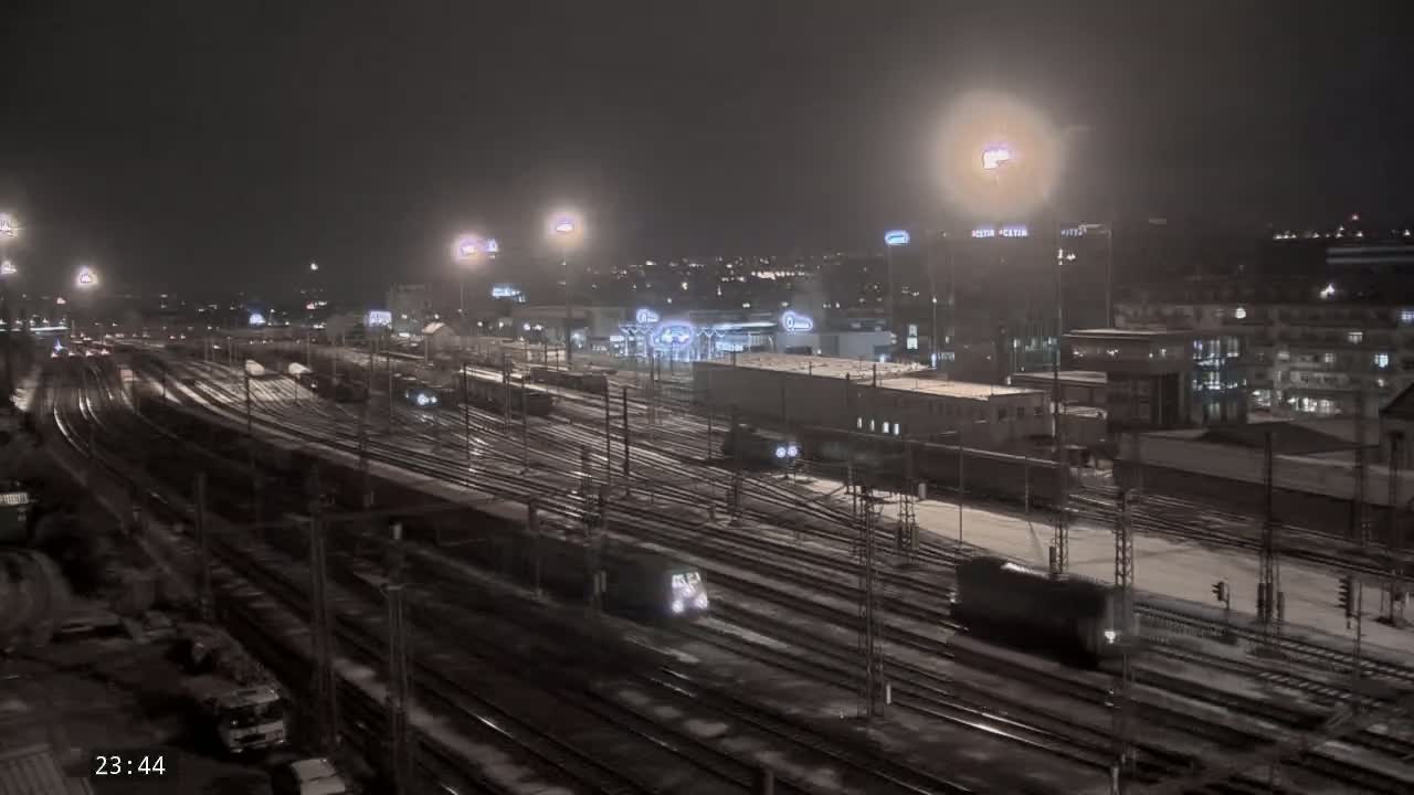 A snow-covered nighttime train yard with multiple trains and tracks illuminated by artificial lights.