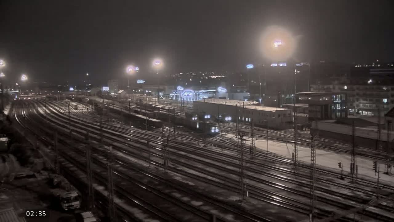 A nighttime view of a snow-covered train yard with numerous tracks and trains, illuminated by bright lights.