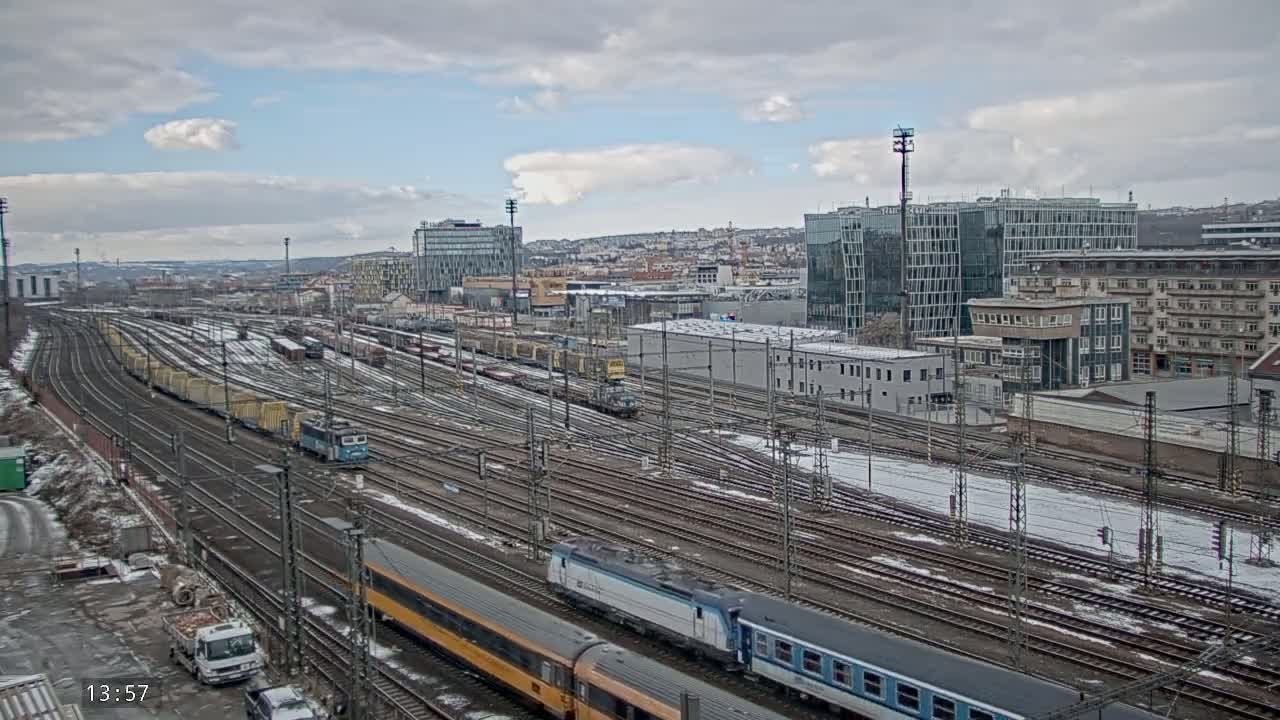 A sprawling railway yard with numerous trains and tracks, partially covered in snow, under a cloudy sky.