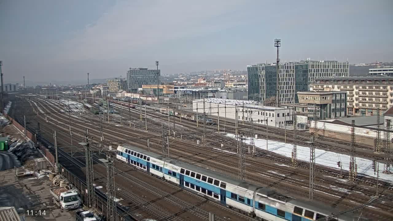 A long train sits in a railway yard on a partly cloudy day with patches of snow on the ground.