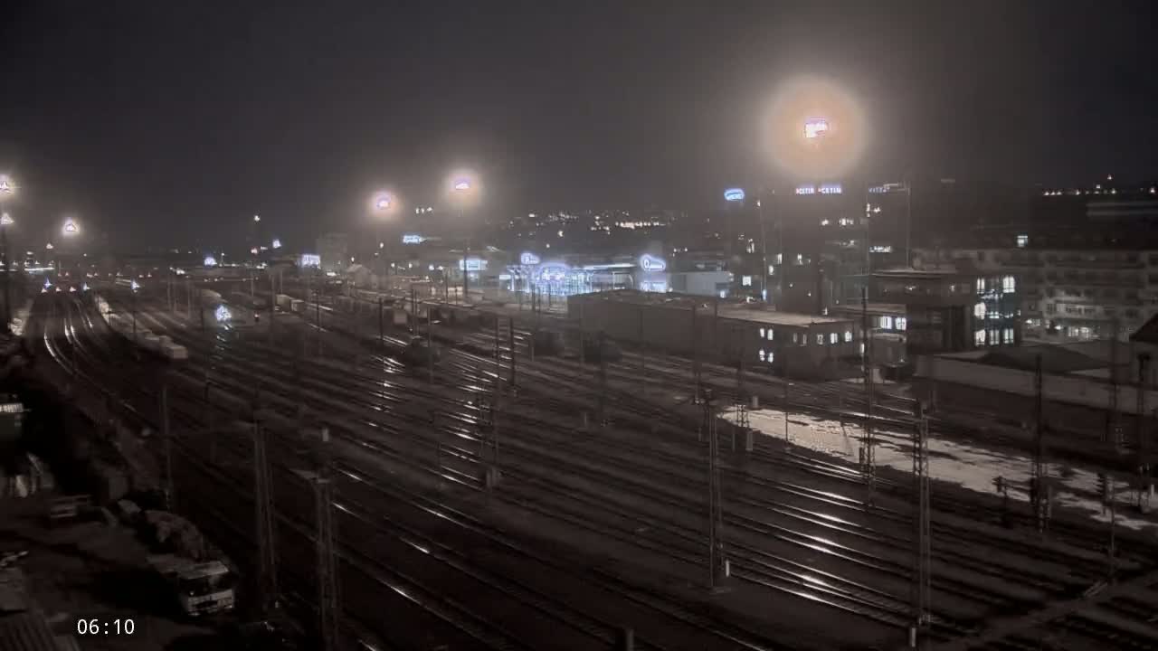A nighttime view of a large train yard with numerous tracks, illuminated by streetlights, under a dark and possibly wet sky.