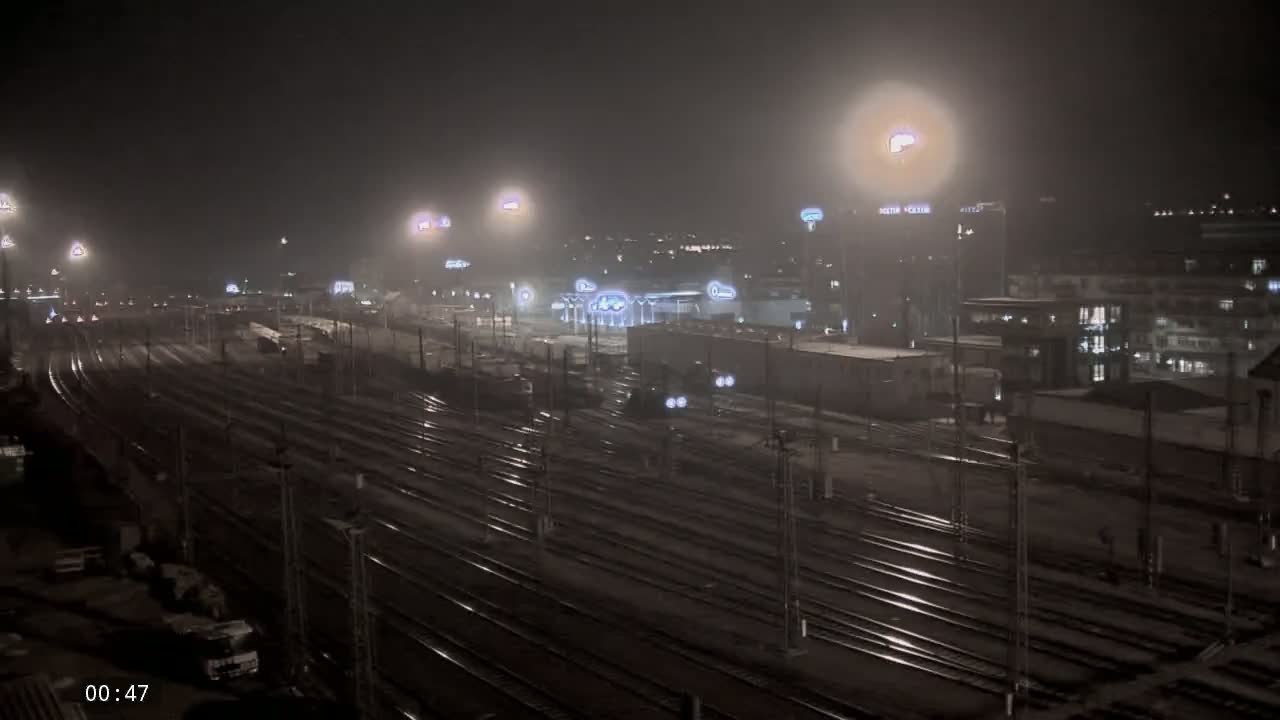 A nighttime view of a train yard with many tracks under hazy or snowy conditions, illuminated by numerous lights.