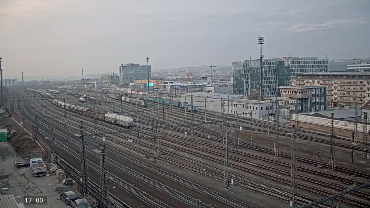 Numerous train tracks stretch toward a city skyline under an overcast sky, with freight trains parked along some of the tracks.