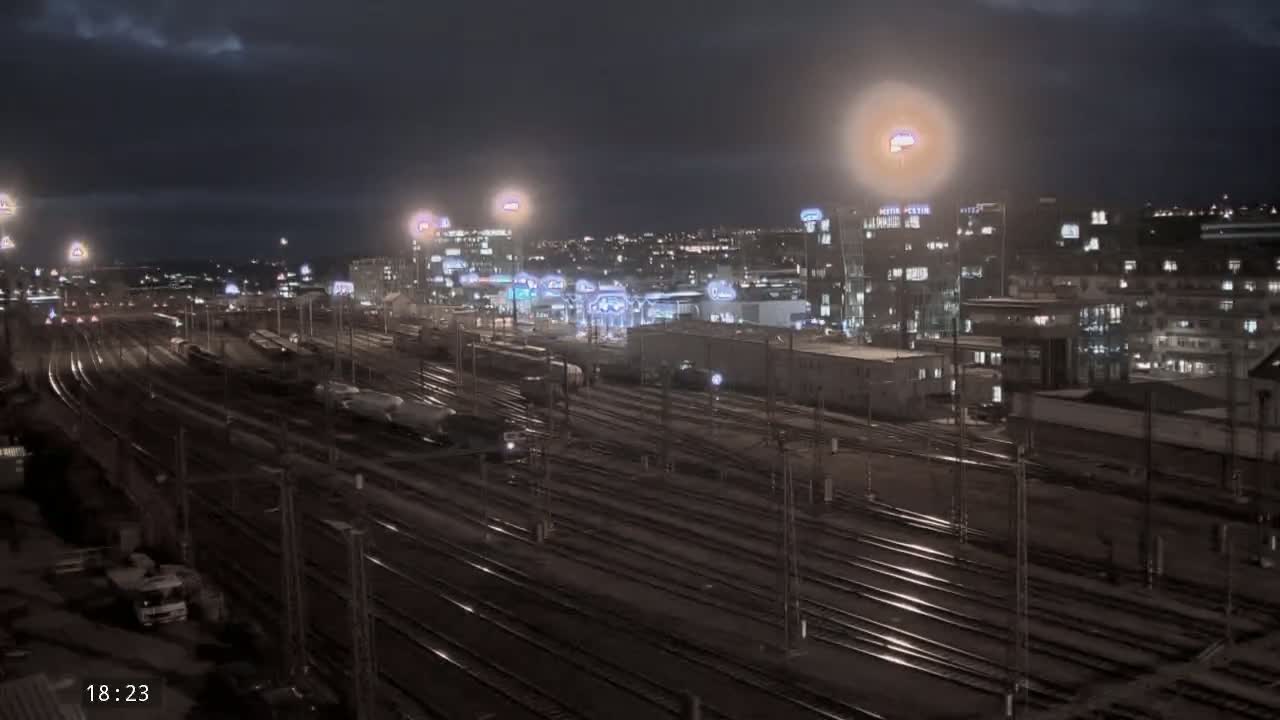 A nighttime view of a sprawling train yard with many tracks, illuminated by artificial lights under a partly cloudy sky.