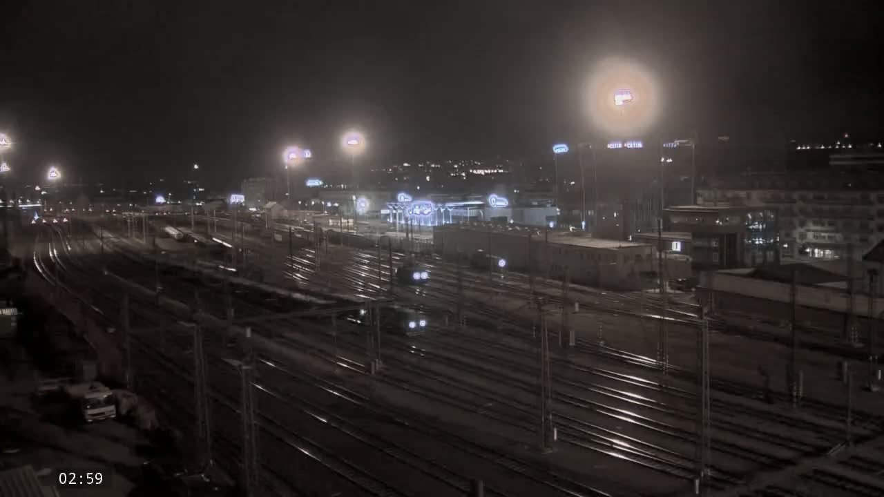 A nighttime view of a sprawling train yard with numerous tracks, illuminated by artificial lights under a dark, possibly snowy sky.