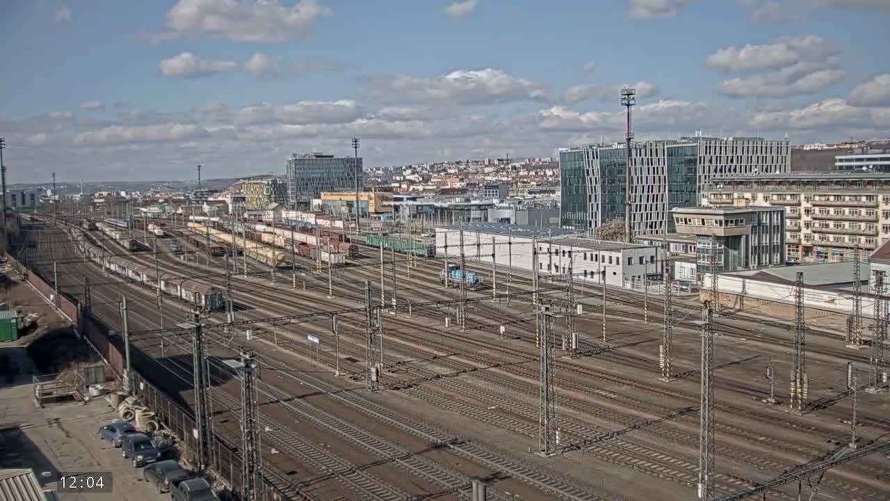 A sprawling railway yard with numerous train cars and tracks under a partly cloudy sky.