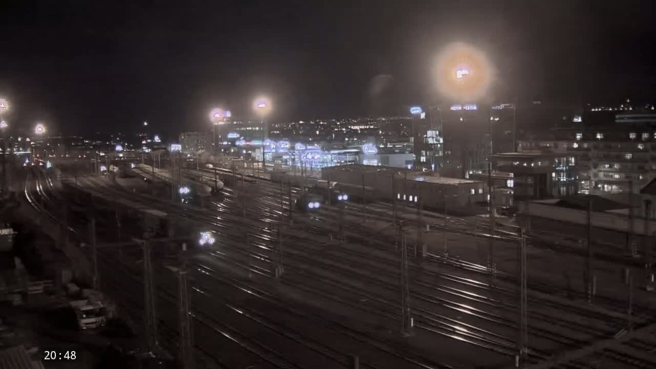 A nighttime view of a sprawling railway yard with trains and buildings illuminated under artificial lights.
