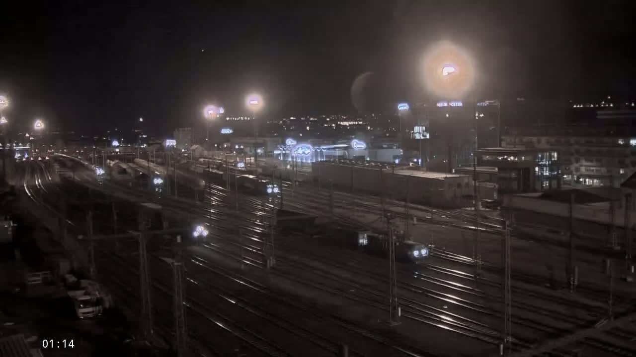 A nighttime view of a train yard with many tracks and trains, illuminated by bright lights under a dark sky.