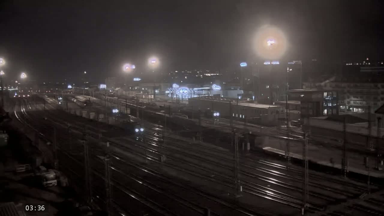 A nighttime view of a railway station and surrounding buildings under hazy conditions, with trains visible on numerous tracks.