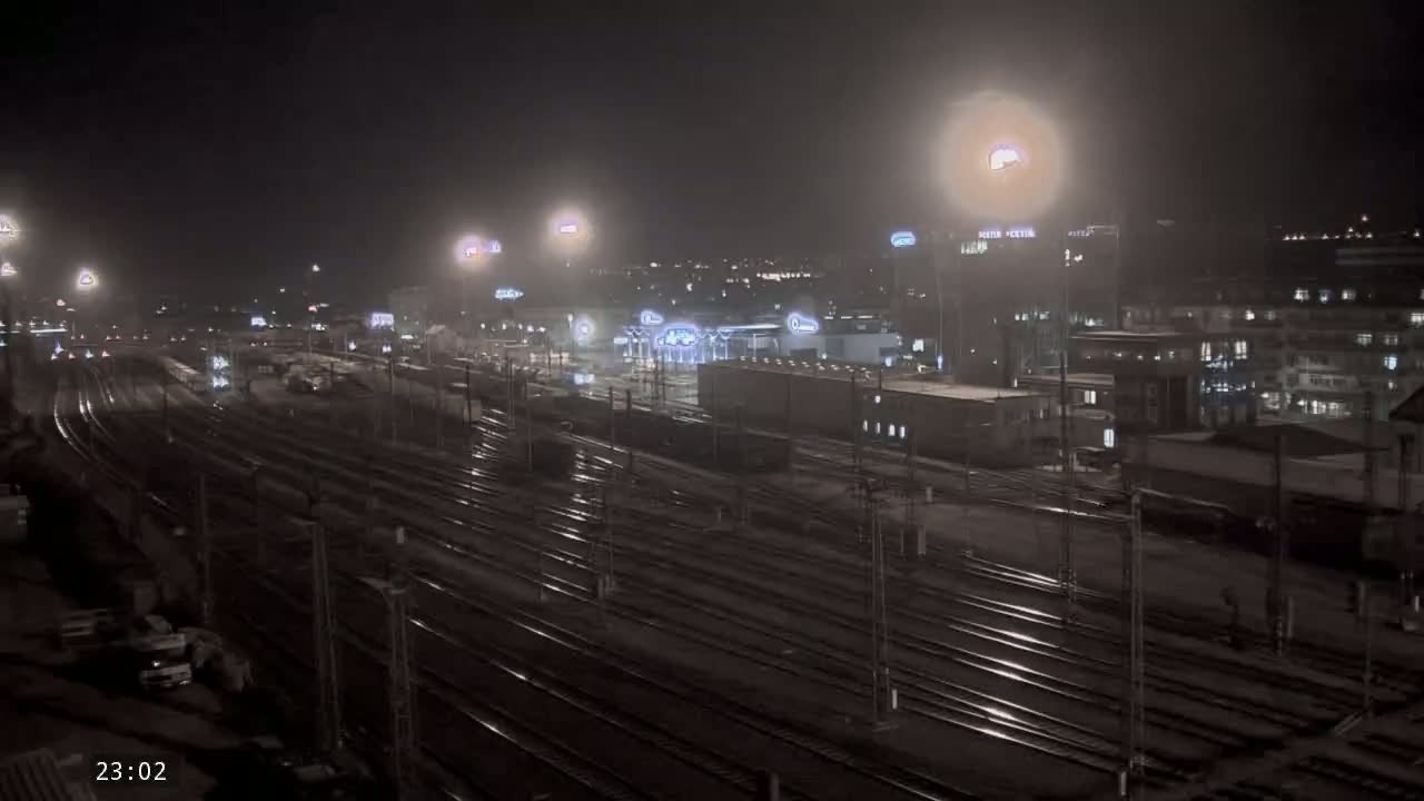A nighttime view of a train yard with many tracks and surrounding buildings under hazy conditions.