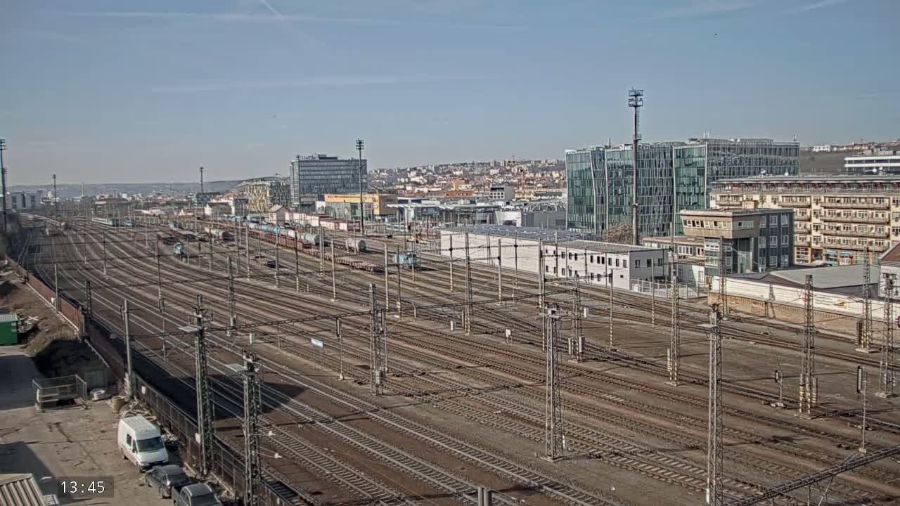 A wide shot of a large railway yard with numerous train tracks, freight cars, and buildings in the background under a mostly clear sky.
