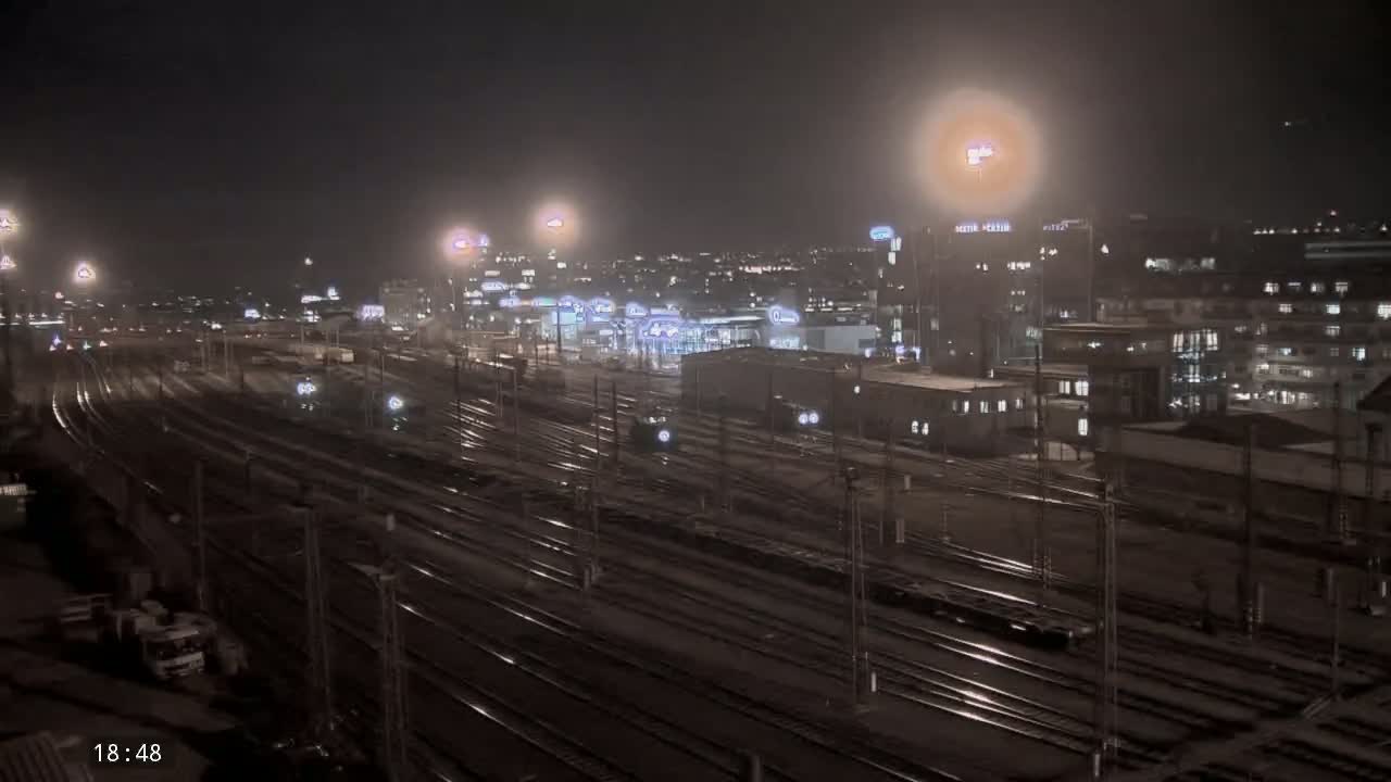A nighttime view of a city's train station and surrounding buildings under hazy conditions.