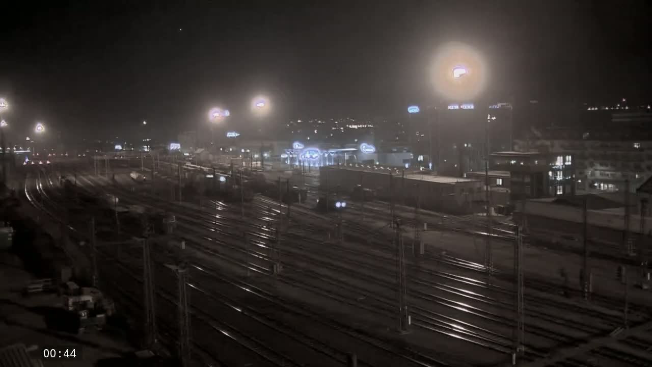 A nighttime view of a sprawling railway yard with numerous tracks illuminated by artificial lights under hazy conditions.