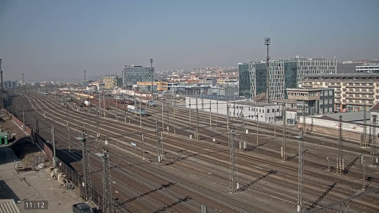 A wide, high-angle view of a sprawling railway yard with numerous tracks and parked freight cars under a clear, sunny sky.