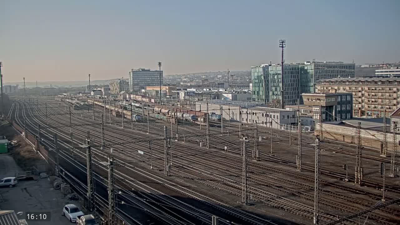 A sprawling railway yard with numerous tracks extends towards a cityscape under a clear, bright sky.