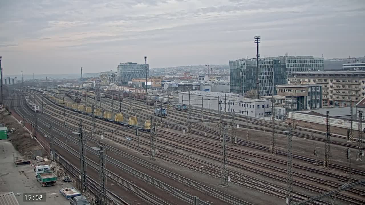 A wide view of a large railway yard with numerous train cars and tracks, under an overcast sky, surrounded by buildings in a city.