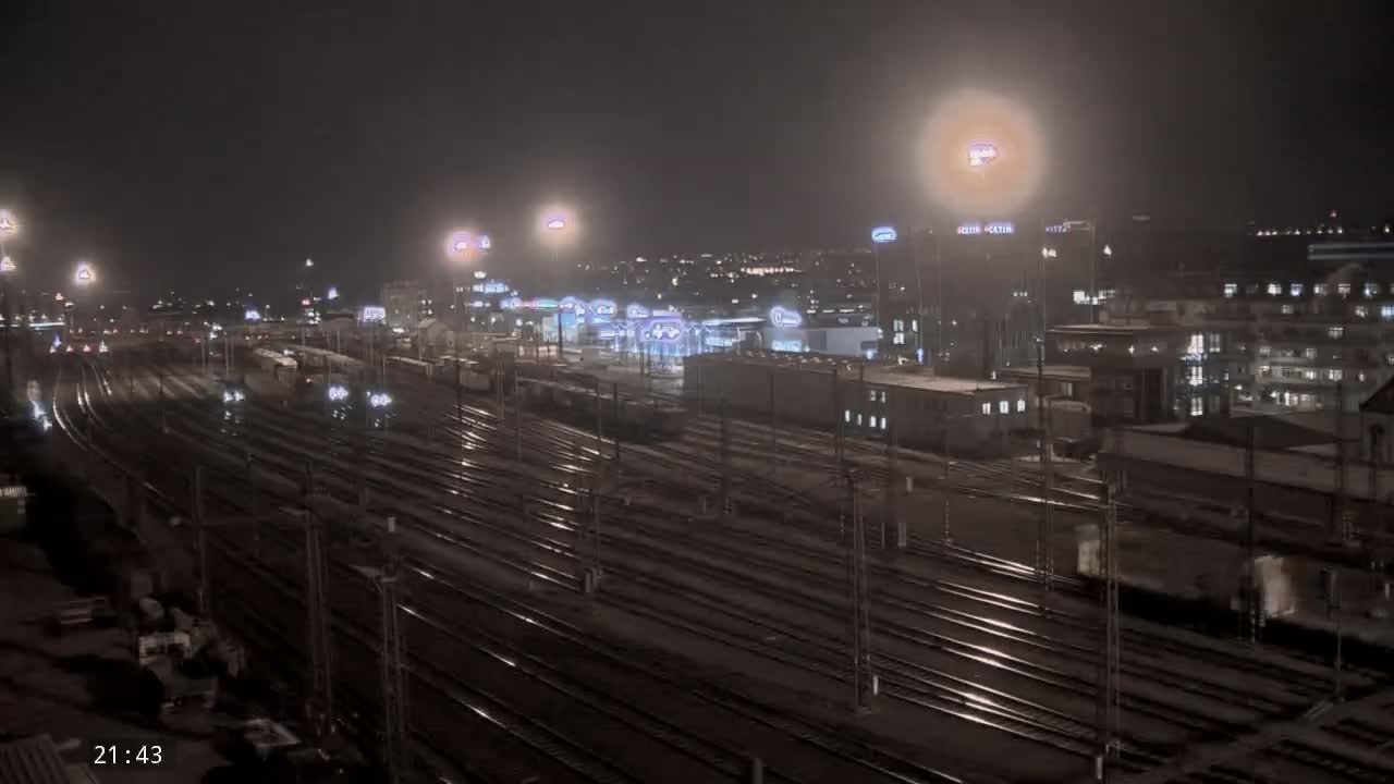 A nighttime view of a large railway yard with many train cars and tracks, illuminated by bright lights under a dark, possibly overcast sky.
