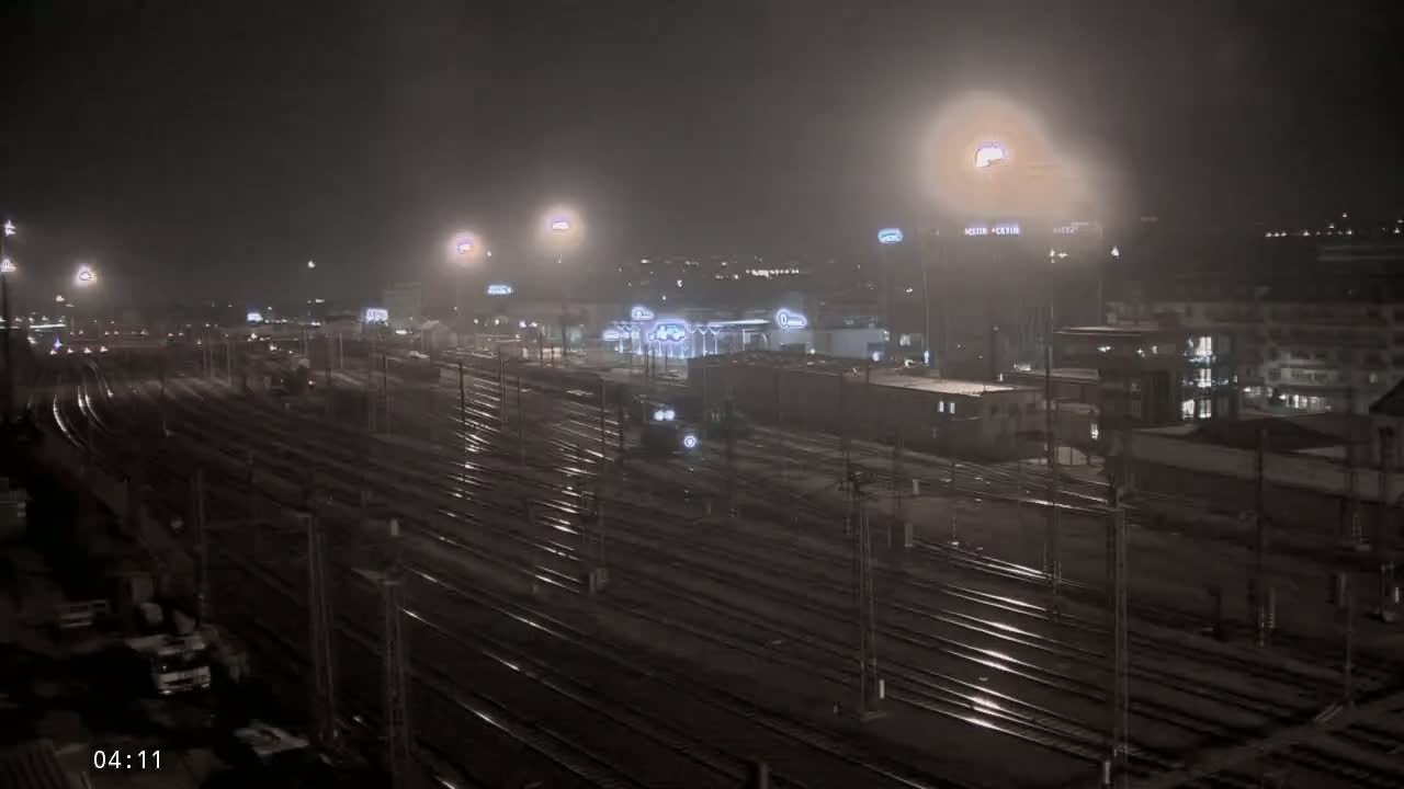 A nighttime view of a sprawling train yard with many tracks under foggy conditions and illuminated by numerous lights.