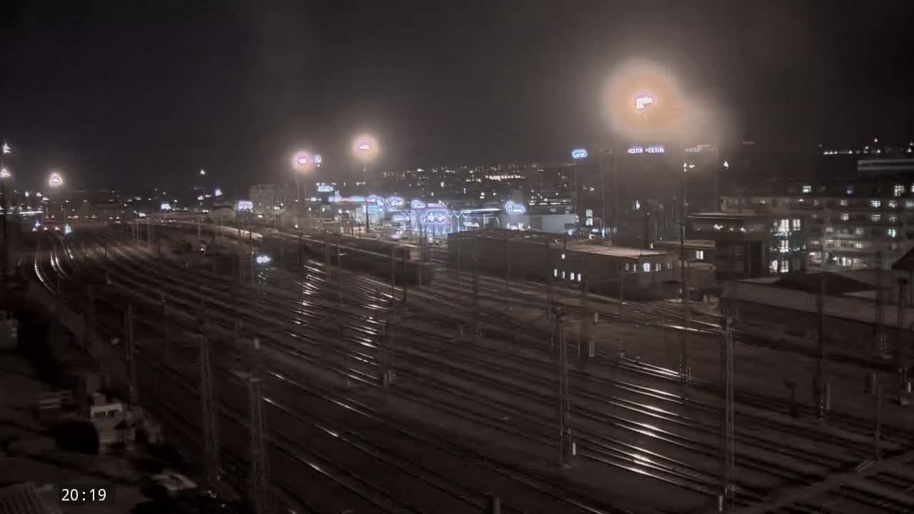 A nighttime view of a sprawling train yard with numerous tracks, illuminated by streetlights, under a dark, possibly overcast sky.