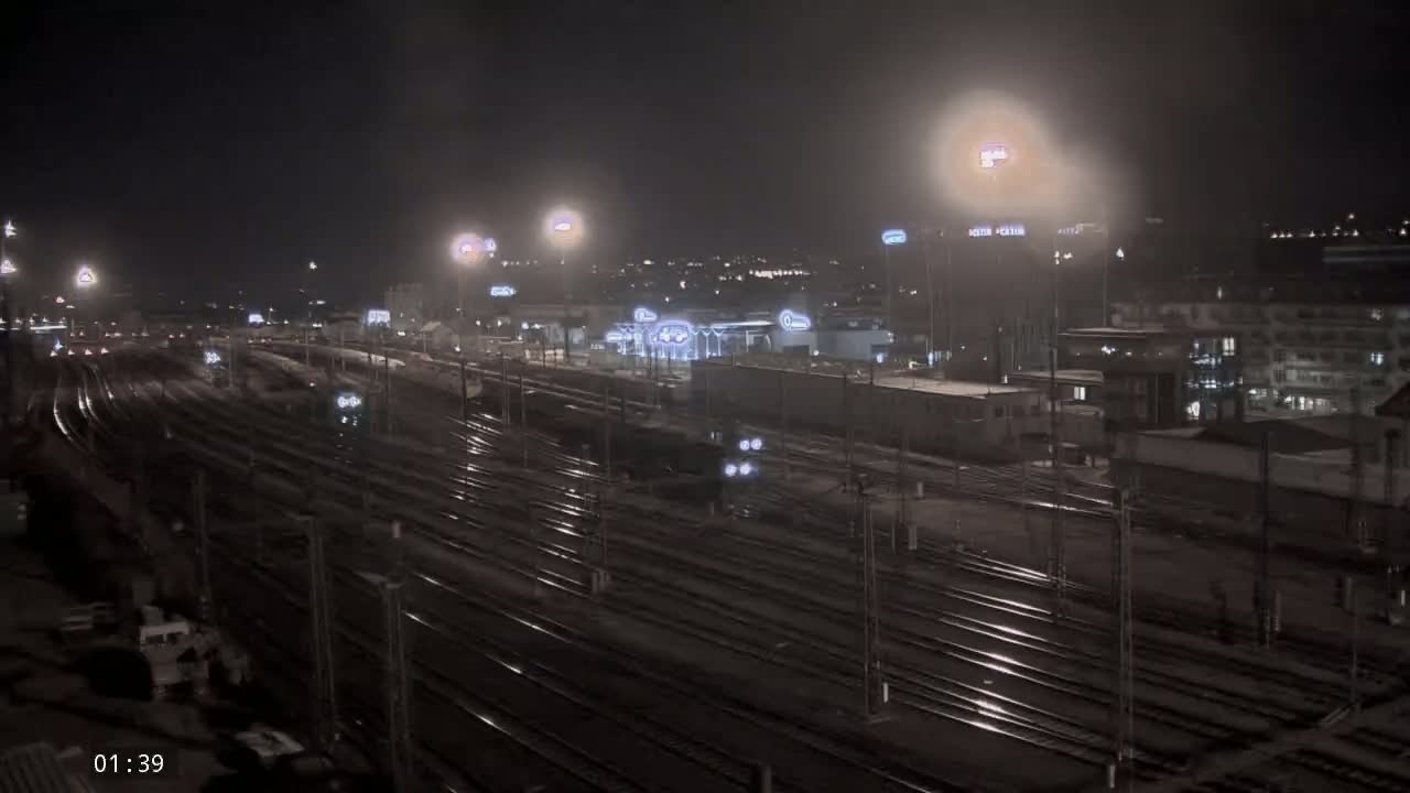 A nighttime view of a sprawling railway yard with numerous tracks, illuminated by artificial lights under hazy conditions.