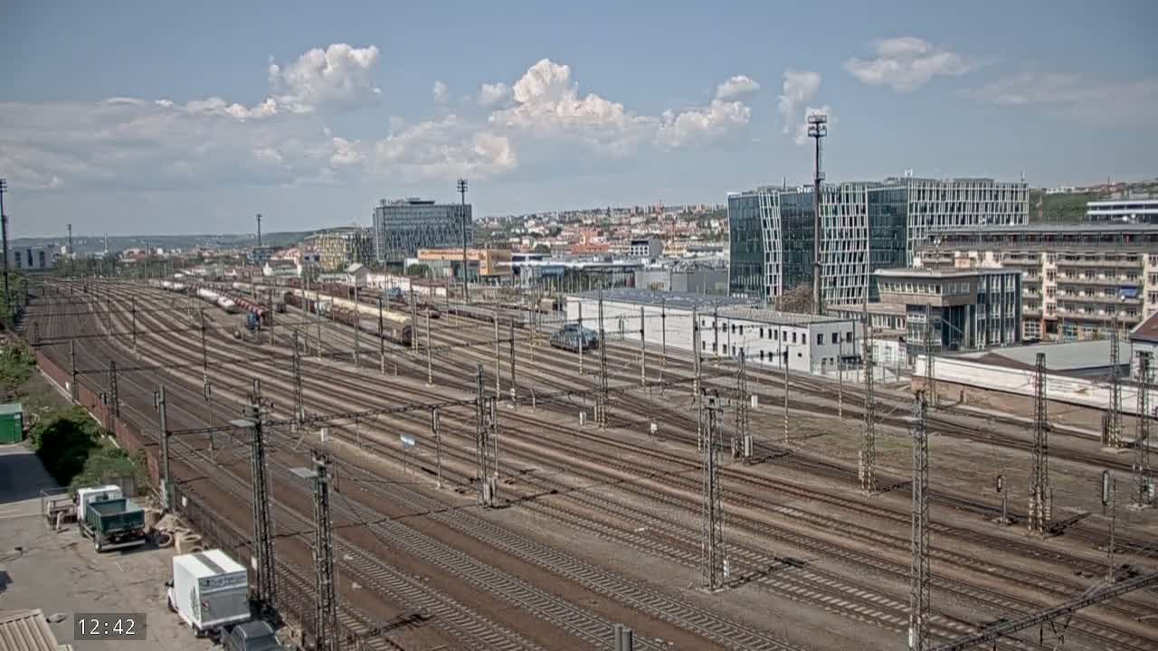 A large railway yard with numerous train cars and tracks stretches out under a partly cloudy sky.