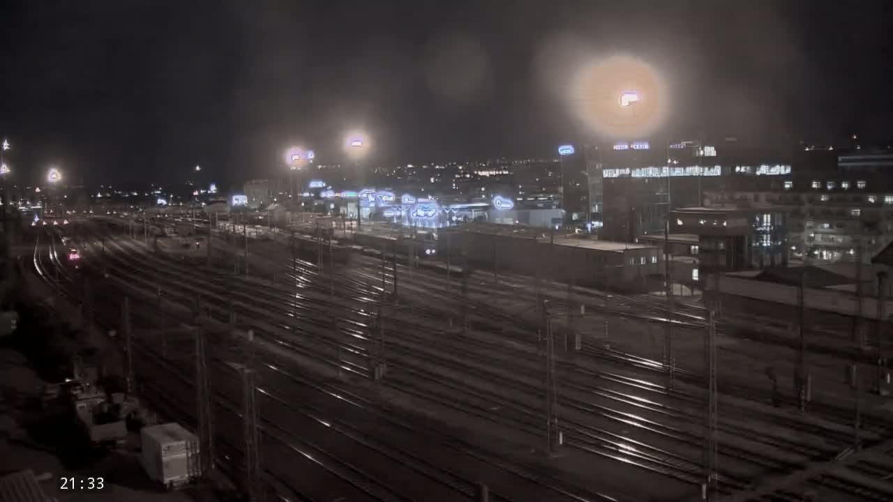 A nighttime view of a sprawling train yard with many tracks, illuminated by artificial lights under hazy or misty conditions.