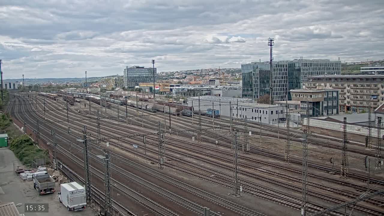 Numerous train tracks extend from a rail yard toward a city skyline under a cloudy sky.
