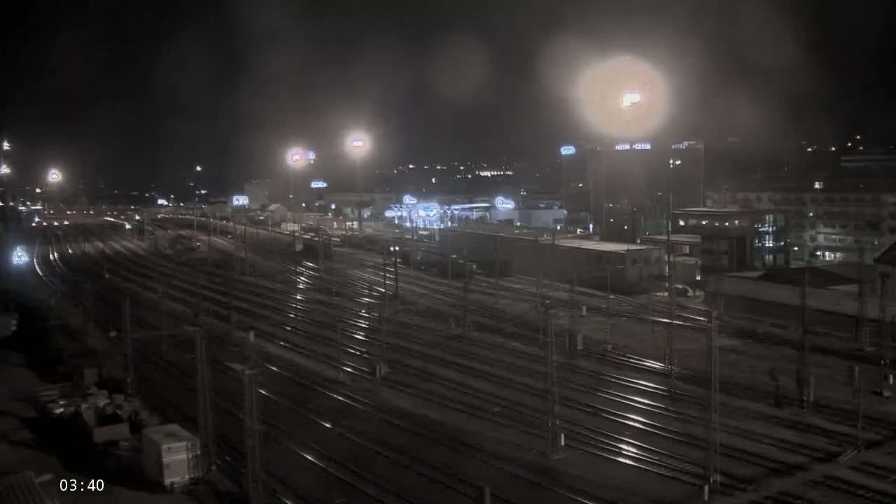 A nighttime view of a wet, expansive train yard with buildings and lights in the background.