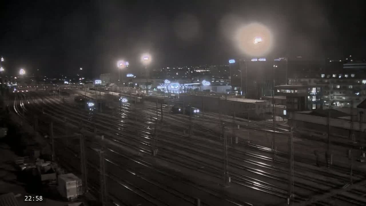 A nighttime view of a sprawling train yard with multiple tracks, illuminated by artificial lights under a hazy sky.