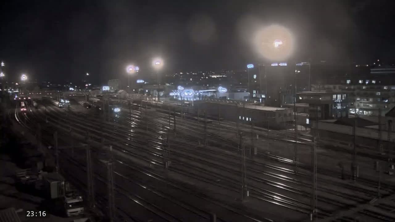 A nighttime view of a sprawling train yard with many tracks, illuminated by lights, under a dark, possibly overcast sky.