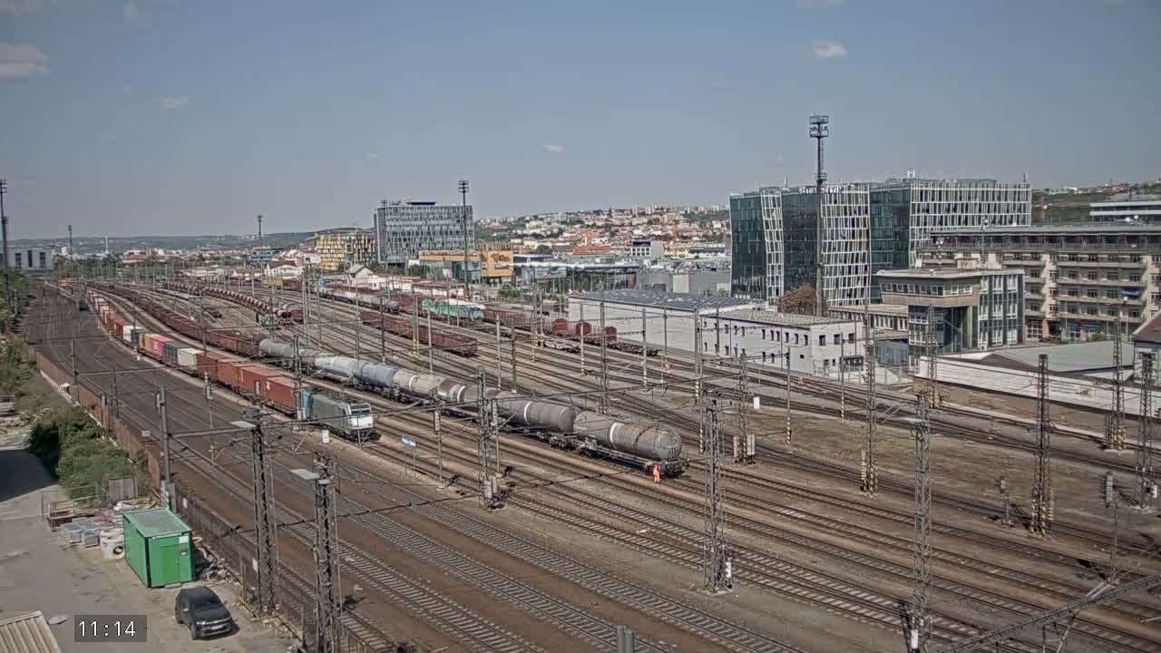 A vast railway yard with numerous freight trains under a clear sky, adjacent to a cityscape.