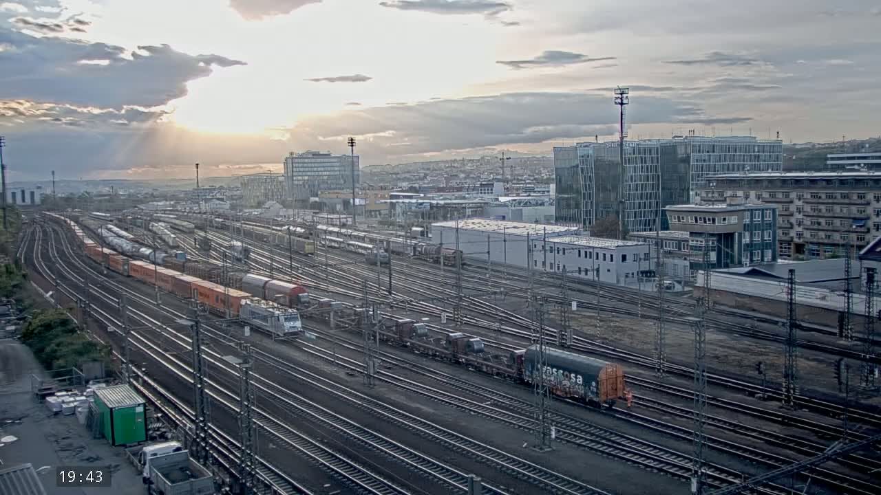 A sprawling railway yard with numerous trains and tracks under a partly cloudy sunset sky.