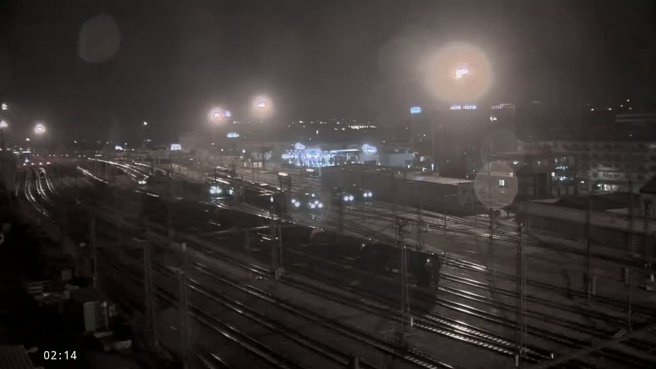 A nighttime view of a railway yard with multiple trains and tracks, under hazy conditions.