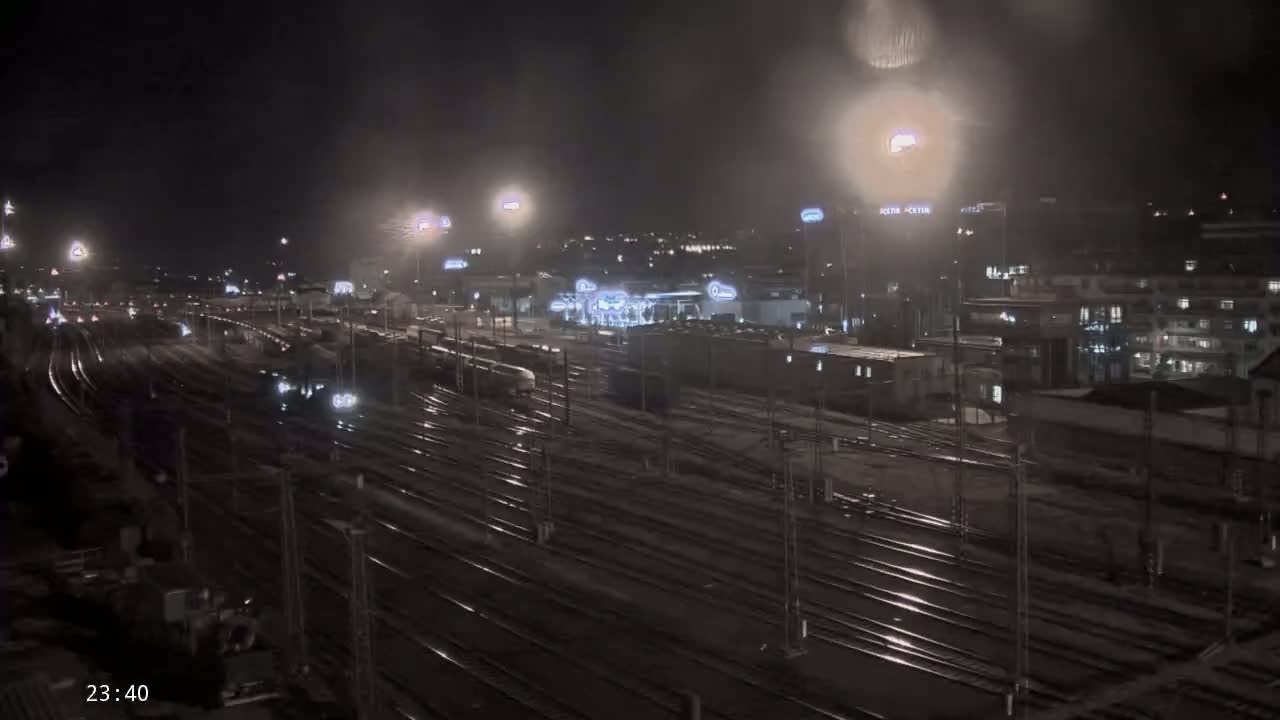 A nighttime view of a sprawling railway yard with numerous train tracks, illuminated by artificial lights under a dark, possibly overcast sky.