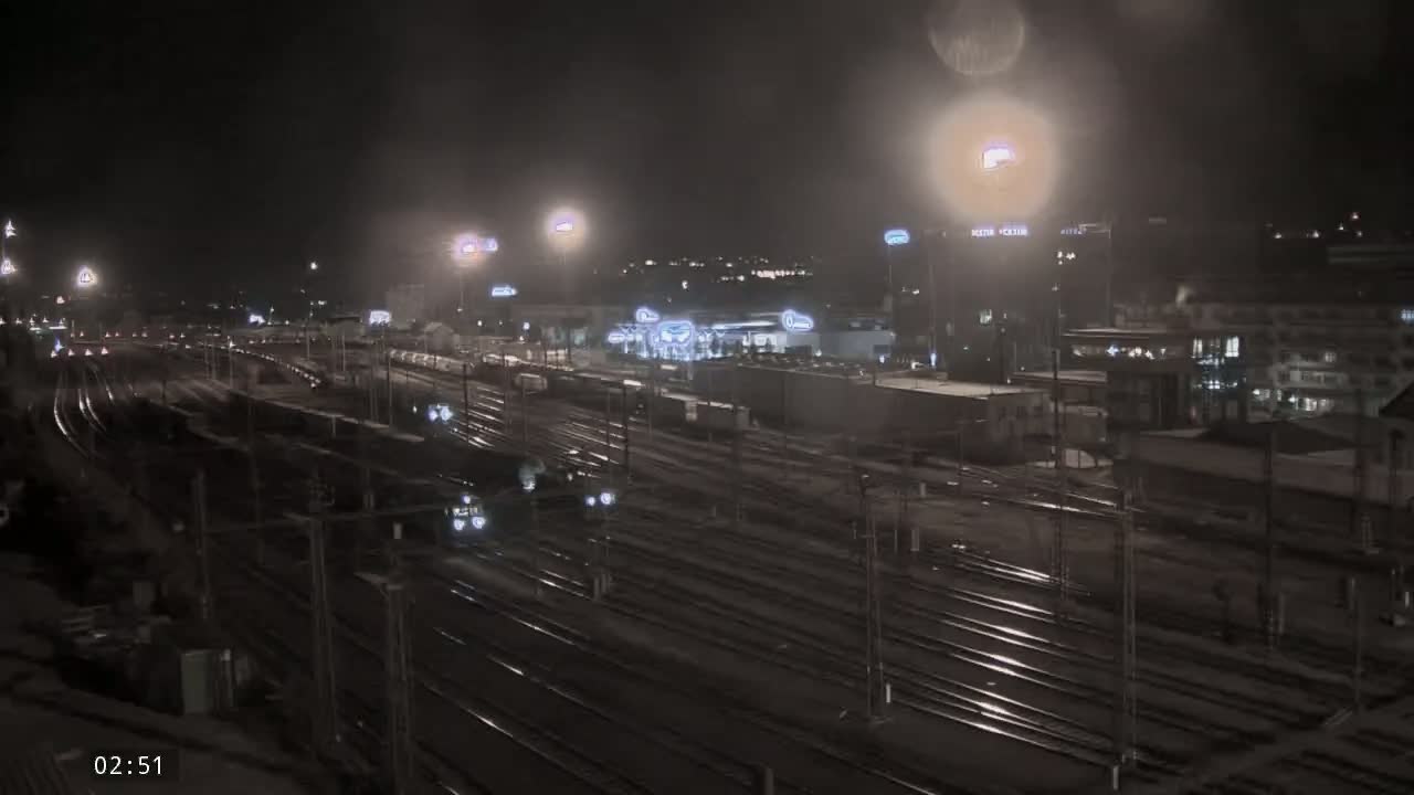 A nighttime view of a sprawling train yard with numerous tracks, illuminated by artificial lights under hazy or foggy conditions.