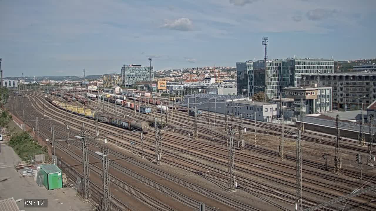 A sprawling railway yard filled with numerous freight cars under a partly cloudy sky.